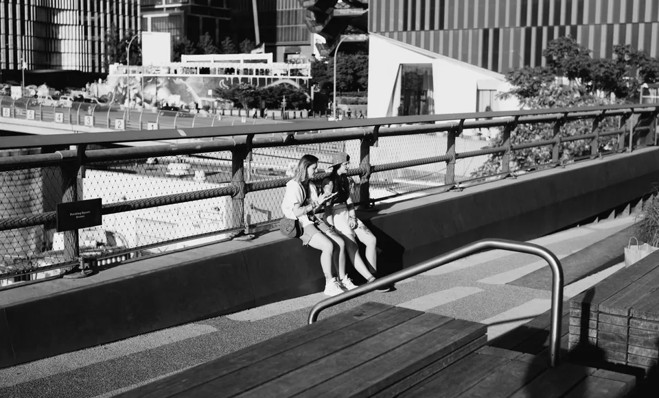 Two people sit beside a railing in a black-and-white photograph, with diagonal shadows across the steps.