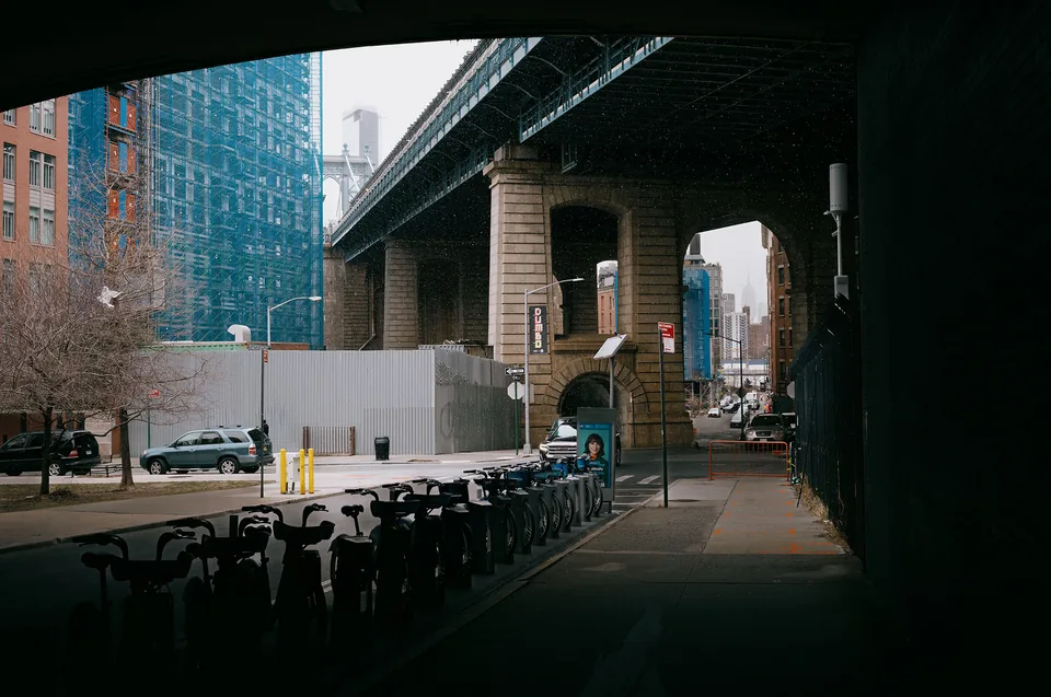 A row of bicycles leads toward the stone arch of a bridge, framed by deep shadows.